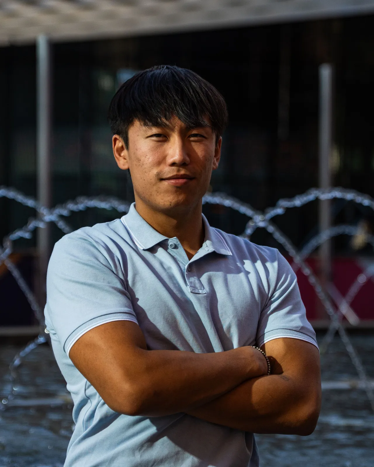 Ziyu mit verschränkten Armen vor einem Brunnen.